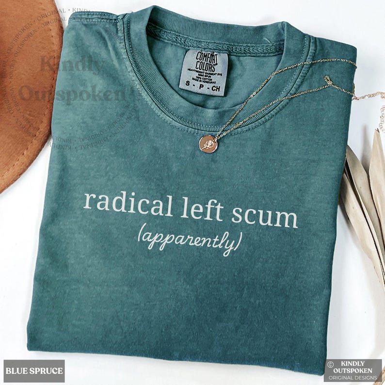 May include: A teal short-sleeve t-shirt with a crew neckline and the text "radical left scum (apparently)" printed in white. The shirt features a Comfort Colors brand label at the inner neck and is paired with a thin gold-tone chain necklace.