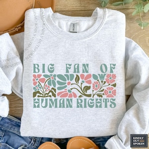 May include: Light gray sweatshirt with the text "BIG FAN OF HUMAN RIGHTS" in green and pink floral design. The sweatshirt is a crew neck style and has a Gildan tag.
