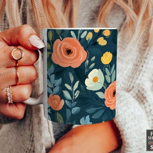 May include: A white ceramic mug featuring a dark teal background decorated with a floral pattern of peach, yellow, and light blue flowers with green leaves. The design covers the exterior surface of the mug, which has a curved handle on the side.
