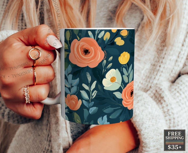 May include: A white ceramic mug featuring a dark teal background decorated with a floral pattern of peach, yellow, and light blue flowers with green leaves. The design covers the exterior surface of the mug, which has a curved handle on the side.