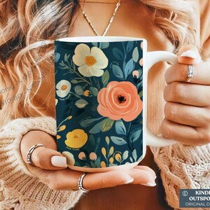 May include: A white ceramic mug featuring a dark teal background with a floral pattern of large peach, cream, and yellow flowers surrounded by green and blue leaves. The text "KINDLY OUTSPOKEN ORIGINAL DESIGNS" is printed in a small box at the bottom.