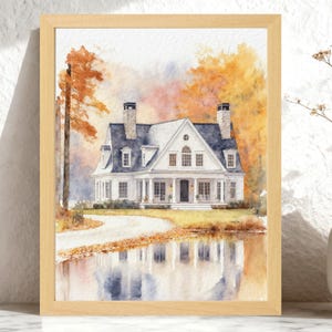 May include: A watercolor painting in a light wood frame depicting a white two-story house with a dark roof and two chimneys. The house is surrounded by autumn trees with orange and yellow foliage, and its reflection is visible in a foreground pond.