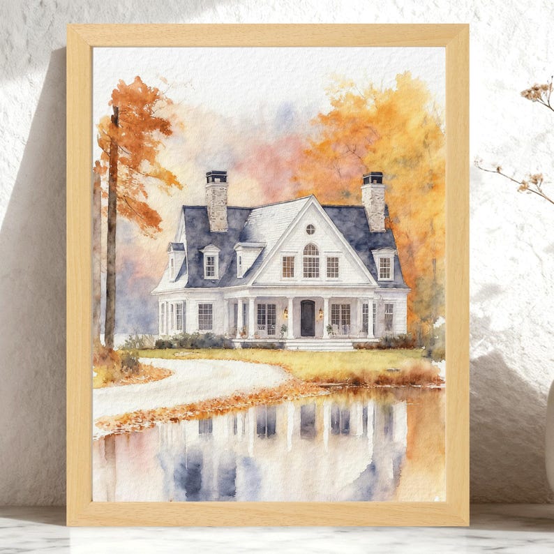 May include: A watercolor painting in a light wood frame depicting a white two-story house with a dark roof and two chimneys. The house is surrounded by autumn trees with orange and yellow foliage, and its reflection is visible in a foreground pond.
