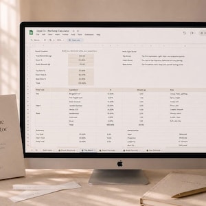 May include: A desktop computer displays a perfume calculator spreadsheet. A book titled "Perfume Calculator" and two scent strips are on the desk. A notebook and pen are also present. The scene is lit with soft, natural light.