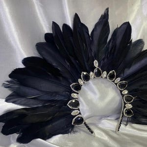 May include: A black feather headdress with a silver and gemstone embellished crown. The headdress features a fan of dark feathers and is adorned with large, teardrop-shaped black gems and smaller clear stones.