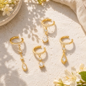 Può includere: Quattro ear cuff dorati con pietre trasparenti sfaccettate. Ogni anello è incastonato con piccole pietre bianche. Un modello presenta una lunga catena con un pendente a goccia marquise, gli altri hanno pendenti a goccia, tondi e a forma di aquilone.