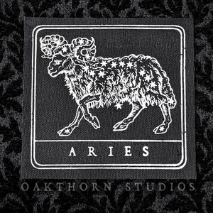 May include: Black and white embroidered patch featuring a stylised ram, the constellation Aries, and the text "ARIES" and "OAKTHORN STUDIOS".
