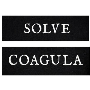 May include: Two black fabric patches with white text. The top patch says "SOLVE" and the bottom patch says "COAGULA".