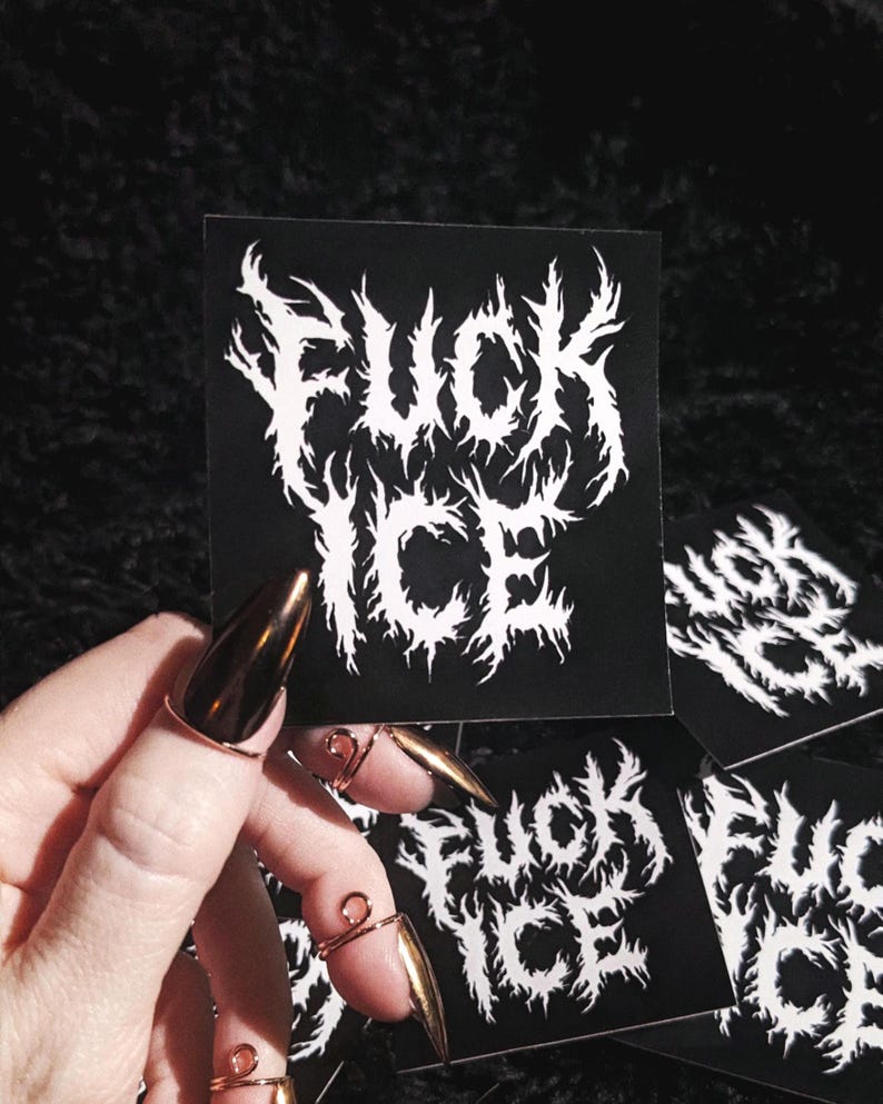May include: Black sticker featuring the words "FUCK ICE" in a white, gothic font. The sticker is held by a hand with long, gold-coloured nails and copper-coloured rings. Several other stickers are visible.