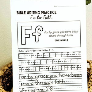May include: A white Bible writing practice sheet with the text "BIBLE WRITING PRACTICE F is for Faith". The sheet includes the letter "F" and a Bible verse. The sheet is in a woven basket.