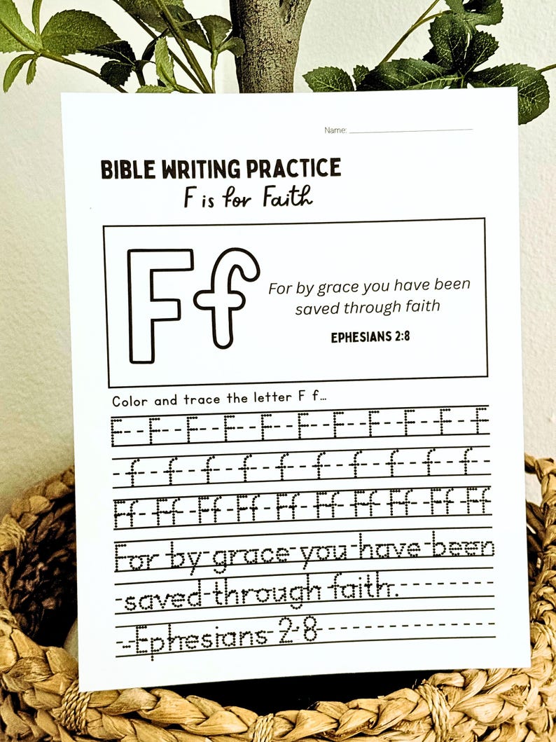 May include: A white Bible writing practice sheet with the text "BIBLE WRITING PRACTICE F is for Faith". The sheet includes the letter "F" and a Bible verse. The sheet is in a woven basket.