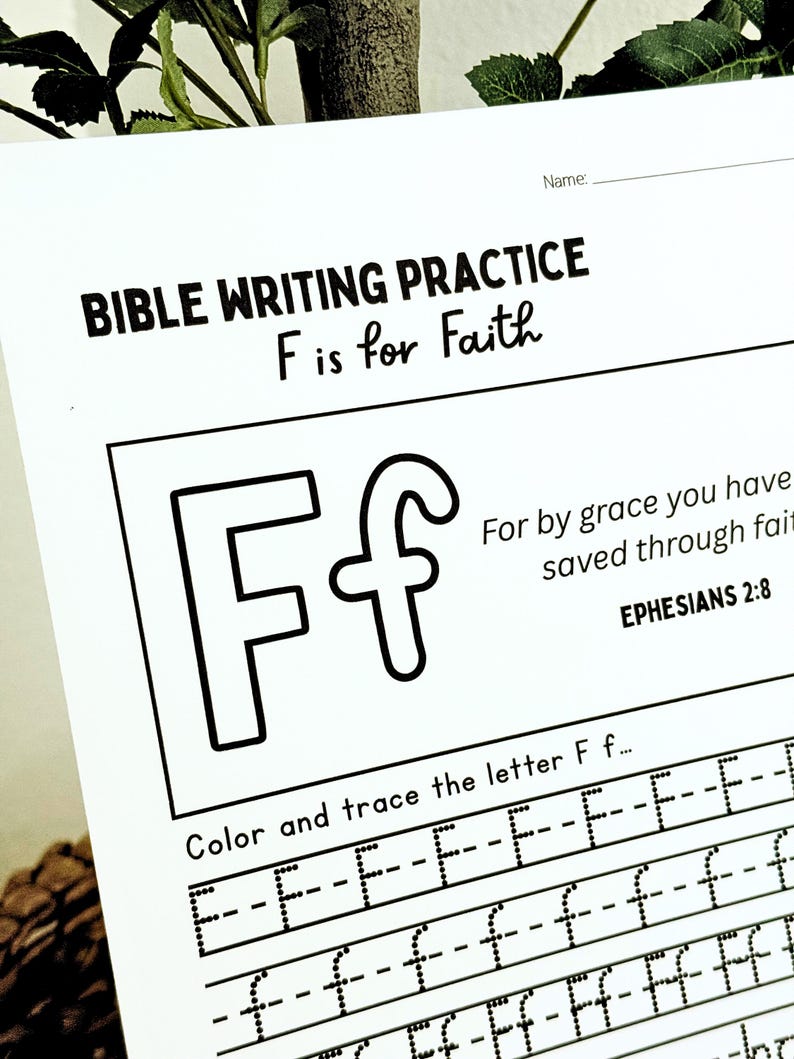 May include: A white Bible writing practice sheet with the text "BIBLE WRITING PRACTICE F is for Faith". The sheet includes a large outlined letter "F" and lines for tracing the letter. The text "For by grace you have saved through faith" is also present.