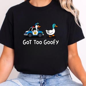 May include: Black t-shirt with a cartoon duck driving a police car and another duck walking. The text "GoT Too Goofy" is printed in white below the graphic. The police car is blue and white with a gold star on the side.