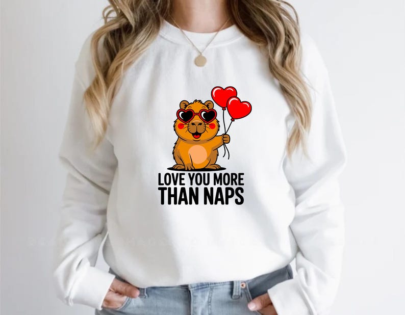 May include: White sweatshirt featuring a cartoon groundhog wearing heart-shaped sunglasses and holding two red heart balloons. The text "LOVE YOU MORE THAN NAPS" is printed below the groundhog in black letters.