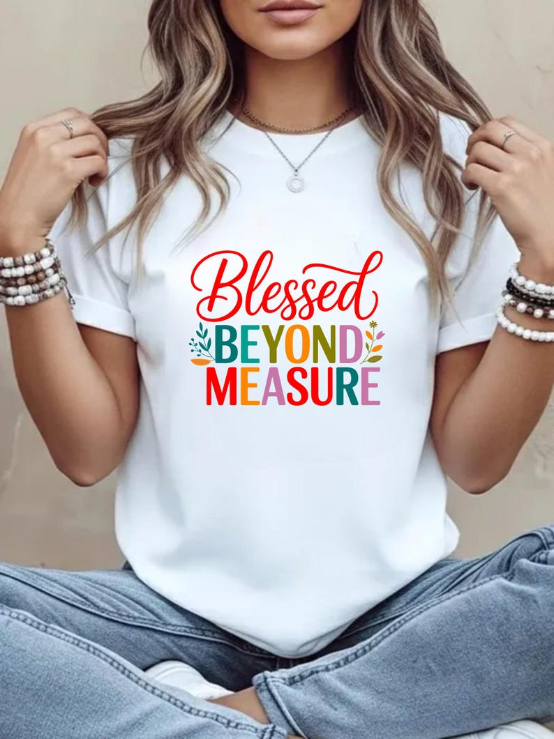 Op de afbeelding: Wit T-shirt met de woorden "Blessed Beyond Measure" in rood, groen, blauw, oranje en paars. Het shirt heeft een ronde hals en korte mouwen. De tekst is in een scriptletter.