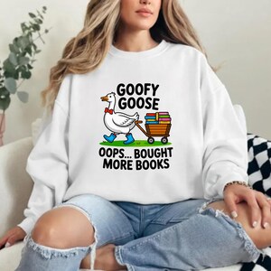 May include: White sweatshirt with a cartoon goose wearing a bow tie and blue boots, pulling a cart of books. The text reads "GOOFY GOOSE" and "OOPS... BOUGHT MORE BOOKS".
