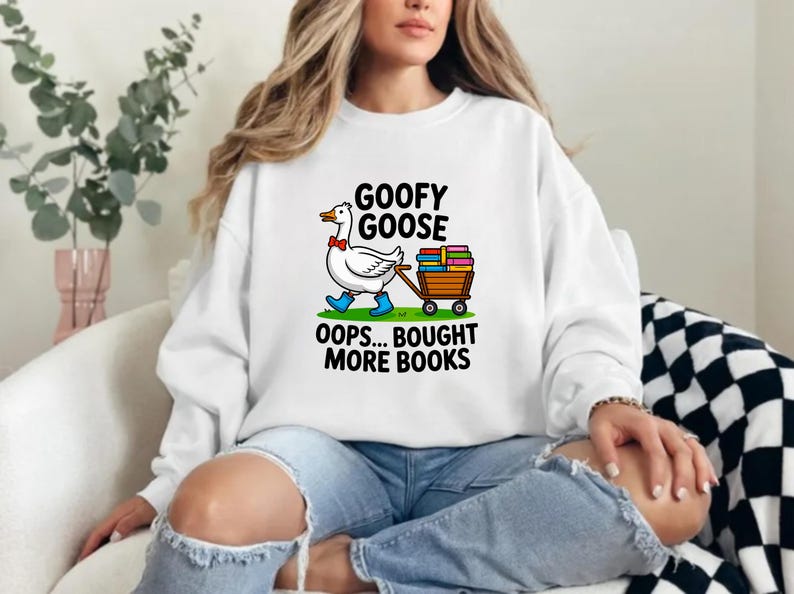 May include: White sweatshirt with a cartoon goose wearing a bow tie and blue boots, pulling a cart of books. The text reads "GOOFY GOOSE" and "OOPS... BOUGHT MORE BOOKS".