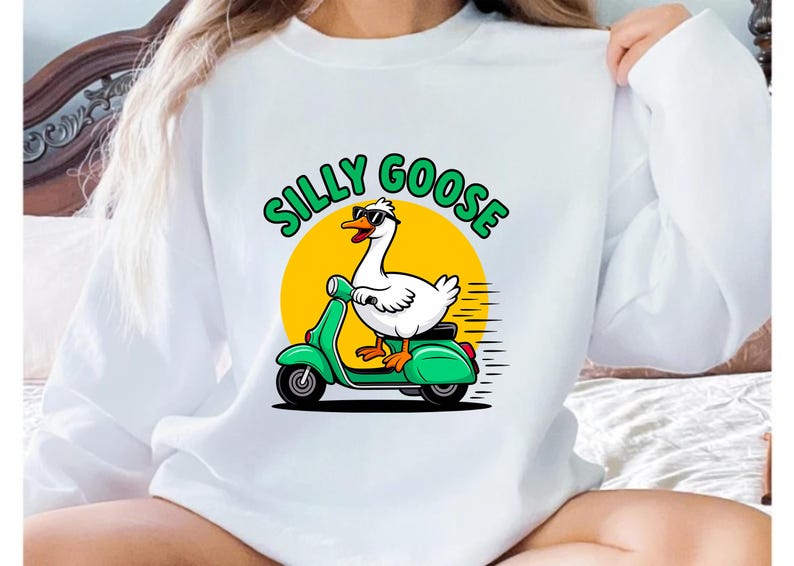 May include: White sweatshirt featuring a cartoon goose wearing sunglasses and riding a green scooter. The text "SILLY GOOSE" is above the goose in green letters with a yellow sun background. A fun, whimsical design.
