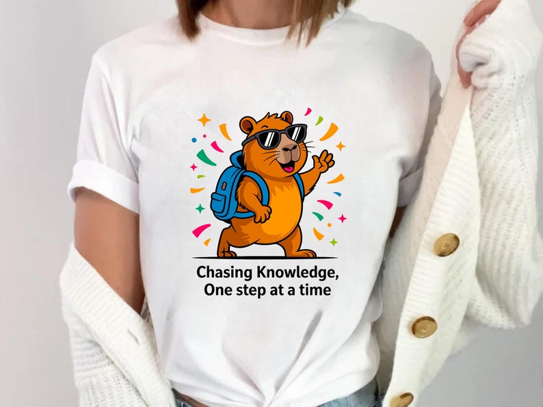 May include: White t-shirt featuring a cartoon groundhog wearing sunglasses and a backpack, waving with its right paw. The groundhog is orange with a blue backpack. The text "Chasing Knowledge, One step at a time" is below the image.