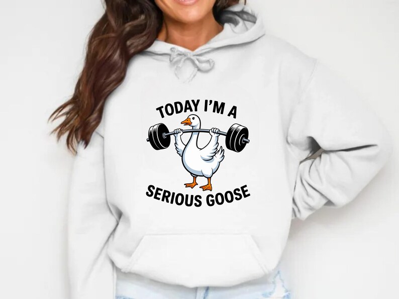 May include: White hoodie featuring a cartoon goose lifting a barbell. The goose is white with orange feet and a yellow beak. Text on the hoodie reads "TODAY I'M A SERIOUS GOOSE".