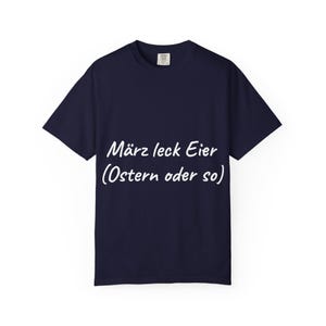 May include: A dark navy blue short-sleeved t-shirt featuring white text printed on the front that reads "März leck Eier (Ostern oder so)". The garment has a classic crew neckline and a standard fit, showcasing a simple design on a solid background.
