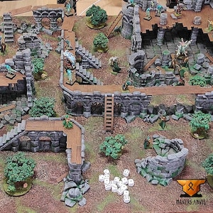 May include: A detailed tabletop gaming terrain set featuring stone ruins, wooden bridges, ladders, and miniature trees. The set includes several miniature figures and dice, all arranged on a brown and green surface. The Makers Anvil logo is visible in the bottom right corner.