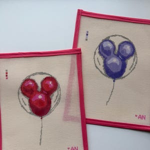 May include: Two needlepoint canvases with a Mickey Mouse balloon design. One balloon is red, the other is purple. Each canvas has a pink border and the initials "AN" in the corner.