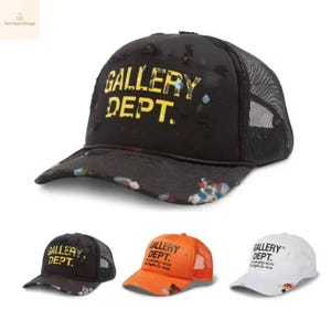 Puede incluir: Gorra de camionero negra con el texto "GALLERY DEPT." en amarillo. La gorra tiene una parte trasera de malla y una visera curva con detalles de salpicaduras de pintura coloridas. También se muestran gorras adicionales en naranja y blanco.