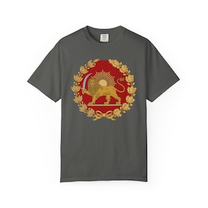 May include: Dark gray t-shirt featuring a circular emblem with a golden lion holding a sword, set against a red background with a sun and laurel wreath design. The shirt is a comfortable, casual wear item.
