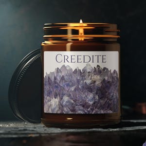 May include: A lit candle in a brown glass jar with a gold lid. The label reads "CREEDITE" above a purple crystal cluster design. The jar is 9oz. and the lid is off to the side.