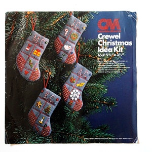 May include: A vintage Crewel Christmas Idea Kit featuring four small, hand-stitched stockings. Each stocking is approximately 2.25 x 3.5 inches and decorated with festive motifs and initials. The kit includes a blue background and red accents.