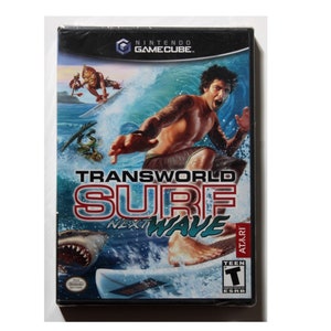 May include: A video game case for the Nintendo GameCube. The game is called "Transworld Surf Next Wave" and features a surfer riding a wave with a shark in the background. The game is rated T for Teen by the ESRB.