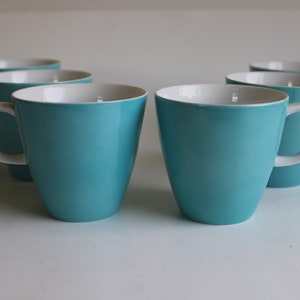 Pu&ograve; includere: Sei tazze in ceramica blu turchese con interno bianco. Le tazze hanno una forma arrotondata e un manico sul lato destro.