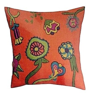 May include: Square decorative pillow with a vibrant orange background and colorful embroidered floral designs. The flowers feature green, pink, blue, and yellow accents, creating a whimsical and artistic aesthetic. The pillow is a square shape.