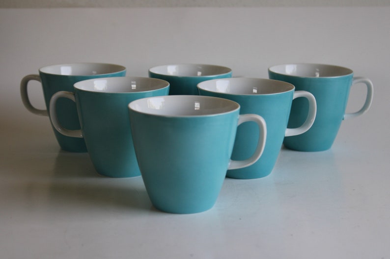 Pu&ograve; includere: Sei tazze in ceramica blu turchese con interno bianco. Le tazze hanno una forma arrotondata e un manico sul lato destro.