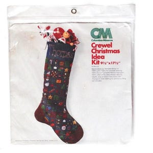 May include: A Christmas stocking kit in a clear plastic bag. The stocking is dark blue with a patterned design and is 9.5 x 17.5 inches. The bag contains small Christmas-themed figurines.