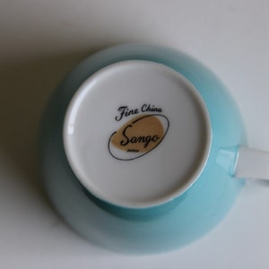Pu&ograve; includere: Una tazza da t&egrave; blu chiaro con interno bianco e un logo dorato e nero che recita "Fine China Sango Japan".
