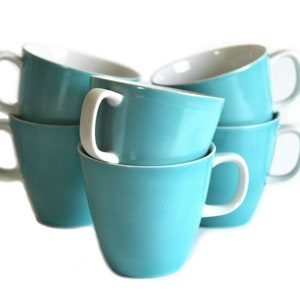 Pu&ograve; includere: Una pila di cinque tazze da caff&egrave; in ceramica turchese con interni bianchi. Le tazze sono impilate a forma di piramide, con la tazza pi&ugrave; grande in basso e la tazza pi&ugrave; piccola in alto.