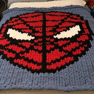 Peut inclure: Une grande couverture bleue faite à la main avec un motif rouge, noir et blanc d'un masque de super-héros. La couverture est faite d'un fil épais et volumineux, idéale pour une chambre confortable.