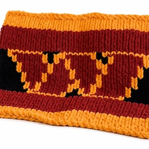 May include: A rectangular knitted cowl featuring horizontal stripes in orange, dark red, and black. The centre section displays a large, stylised letter W pattern created with orange yarn against a dark red and black background.