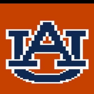 Może przedstawiać: Pikselowy wz&oacute;r z literami "A" i "T" w kolorze granatowym i białym, na pomarańczowym tle. Projekt przypomina logo uczelni, z odważną, blokową czcionką.