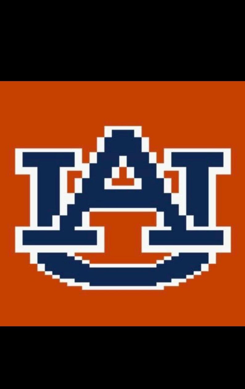 Może przedstawiać: Pikselowy wz&oacute;r z literami "A" i "T" w kolorze granatowym i białym, na pomarańczowym tle. Projekt przypomina logo uczelni, z odważną, blokową czcionką.