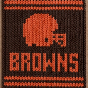 May include: A rectangular knitted textile featuring a dark brown background with orange horizontal stripes at the top and bottom. The center displays an orange knitted football helmet graphic above the orange text BROWNS in block letters.