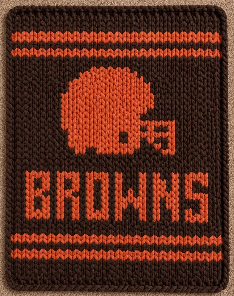 May include: A rectangular knitted textile featuring a dark brown background with orange horizontal stripes at the top and bottom. The center displays an orange knitted football helmet graphic above the orange text BROWNS in block letters.