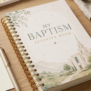 Könnte beinhalten: Ein spiralgebundenes "My Baptism Activity Book" mit goldfarbenen Spiralen. Das Cover zeigt eine Aquarellillustration einer Kirche, Berge und den Text "My Baptism Activity Book". Ein goldener Stift und ein Aquarellset sind ebenfalls zu sehen.