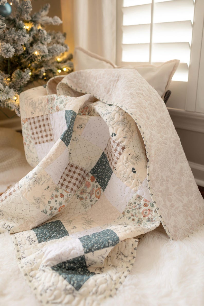 May include: A patchwork quilt featuring a variety of square fabric blocks in shades of sage green, cream, and brown. The design includes floral patterns, small polka dots, and a brown gingham check, all finished with a quilted texture and floral border.