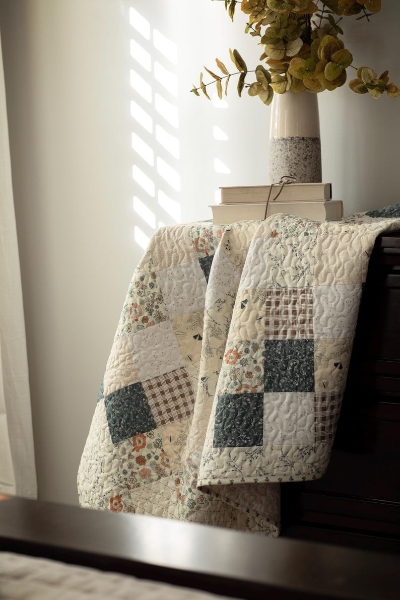 May include: A patchwork quilt featuring a variety of square fabric blocks in cream, dark green, and brown tones. The quilt displays a mix of floral patterns, small-scale geometric prints, and solid colors, all finished with a continuous swirling stitch.