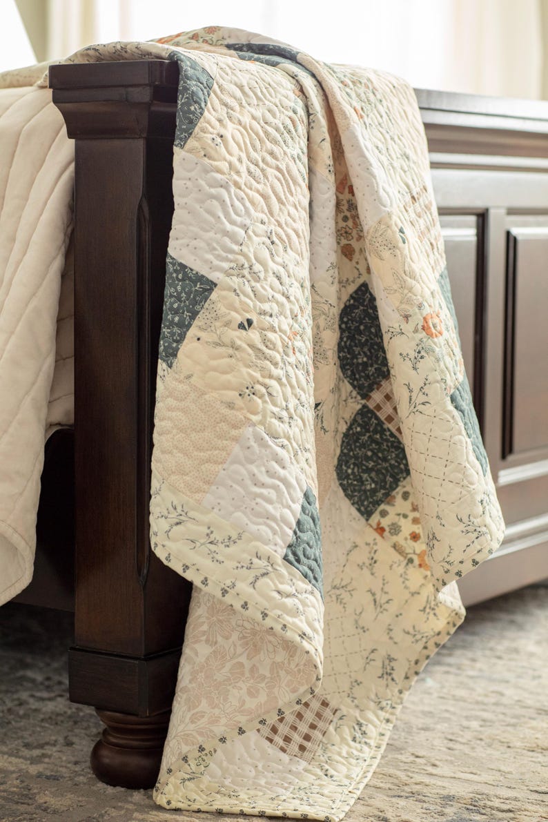 May include: A patchwork quilt featuring a variety of square fabric blocks in cream, sage green, and muted orange tones. The quilt displays floral, botanical, and plaid patterns with a textured, quilted stitch finish draped over a dark wood bed frame.