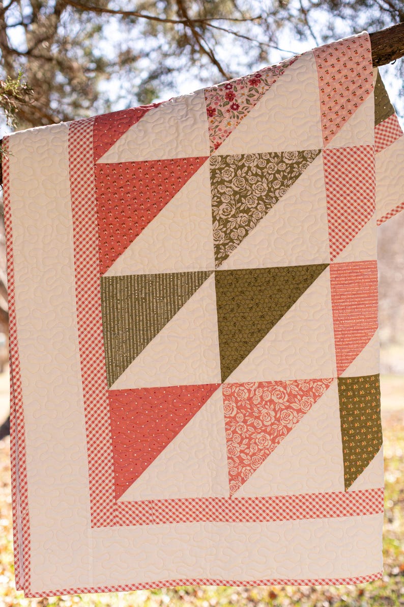 May include: A patchwork quilt with a variety of patterns and colours. The quilt features coral, olive green, and floral patterned triangles, set against a white background. The border is a red and white gingham pattern.