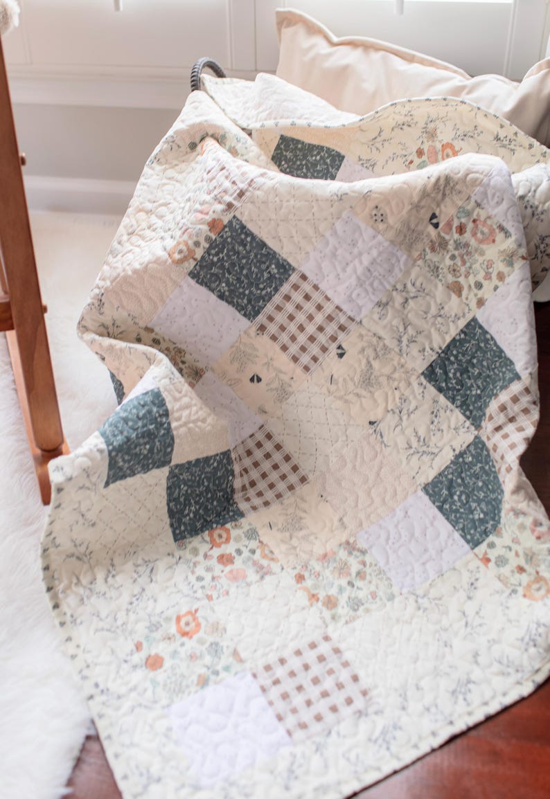 May include: A patchwork quilt featuring a variety of square fabric blocks in muted tones of sage green, cream, and brown. The design includes floral patterns, small-scale gingham checks, and solid cream squares, all finished with a quilted texture.
